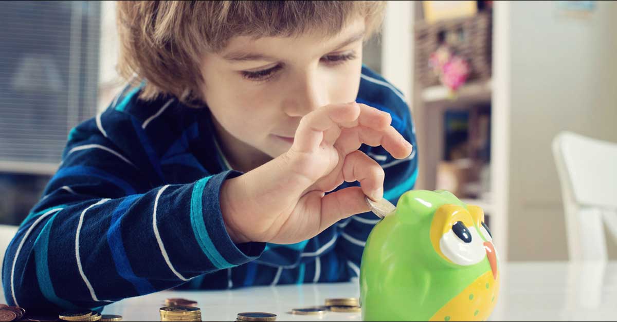 Young boy in a blue striped shirt placing a coin into a green and yellow owl coin bank