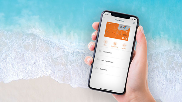 A hand holding a phone with the bcu Connect App open. The background is the ocean.